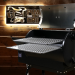 Black grill with open lid on a wooden background featuring a PMG logo.