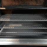Open grill with two mesh racks inside, showing signs of use.