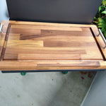 Wooden cutting board on a stand with a plant in the background