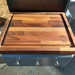 Wooden cutting board on a grill with a brand logo.
